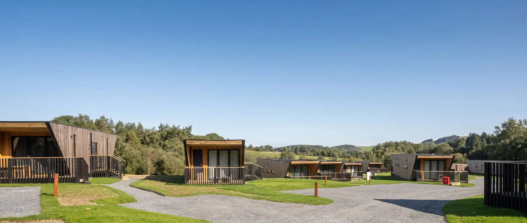 Row of contemporary angular timber lodges beside a gravel path and woodland